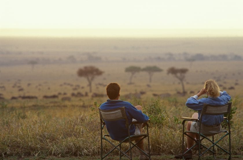 She looks off to distant scene of wildebeest herd with binoculars