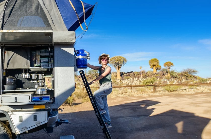 Woman tourist on safari travel vacation in Africa, young girl near camping car with tent and kitchen in camp, quiver tree forest, Namibia