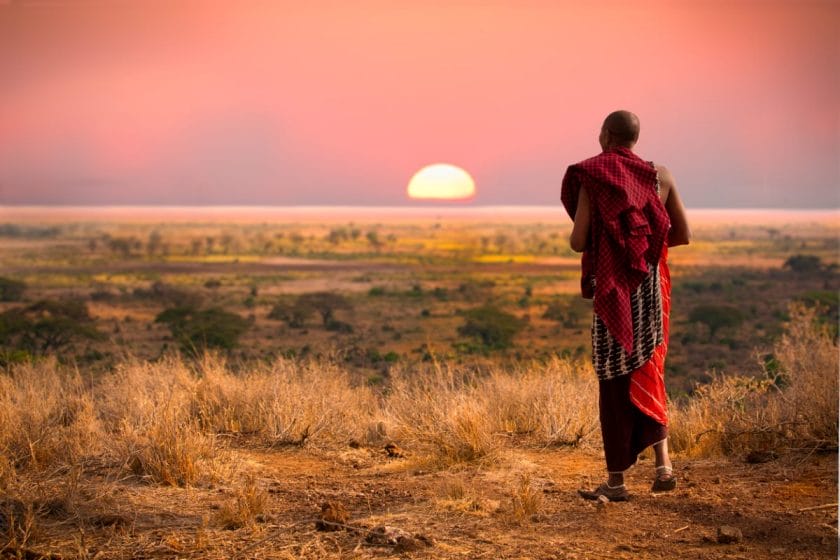 A Masai warrior walks through the bush during sunset.
